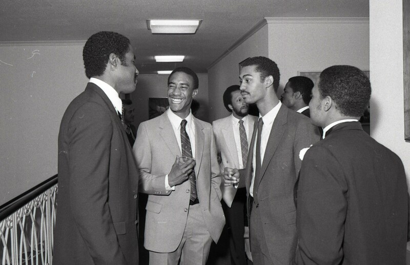 Several young men talking and laughing in suits.