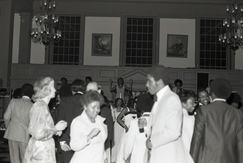 Students dancing to music being performed live in Evans Hall at the 1977 Black Ball at Washington and Lee University. The performers are visible in the background of the photograph.