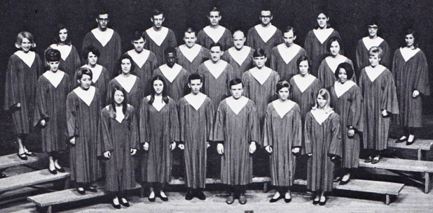 A group of about 24 students standing on a stage wearing choir robes