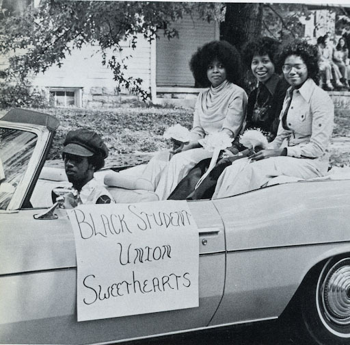 Three female Centre College students, representing the Black Student Union, riding on the back of a convertible during a parade