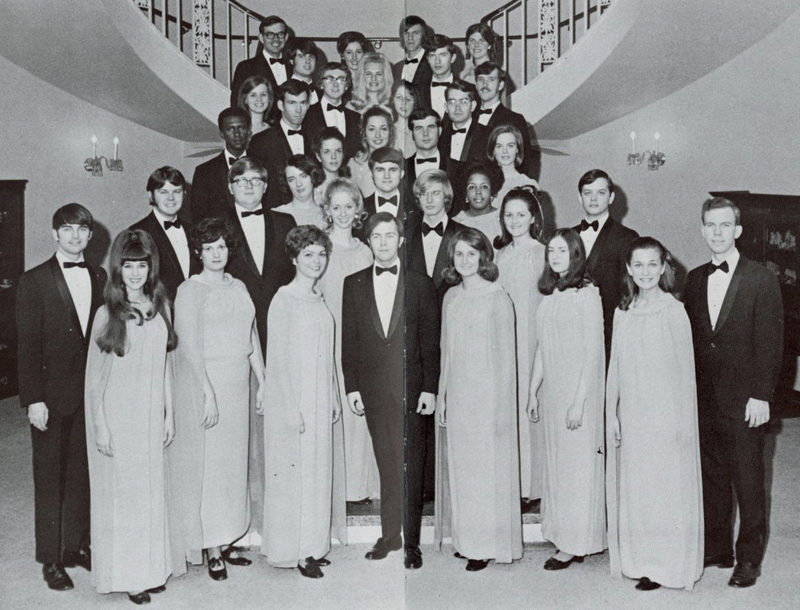 A group of about 30 students standing on stairs wearing formal gowns and suits.